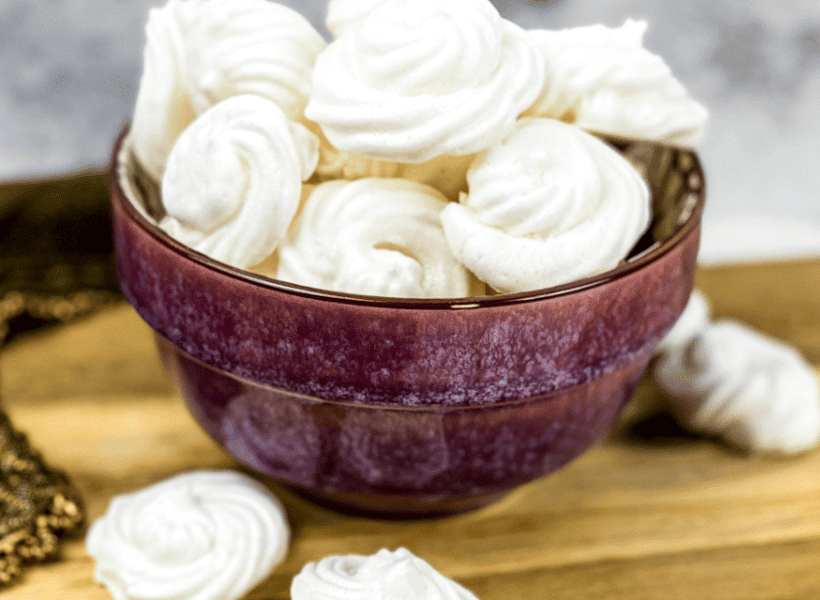bowl of meringue cookies and a few beside the bowl on wood cutting board