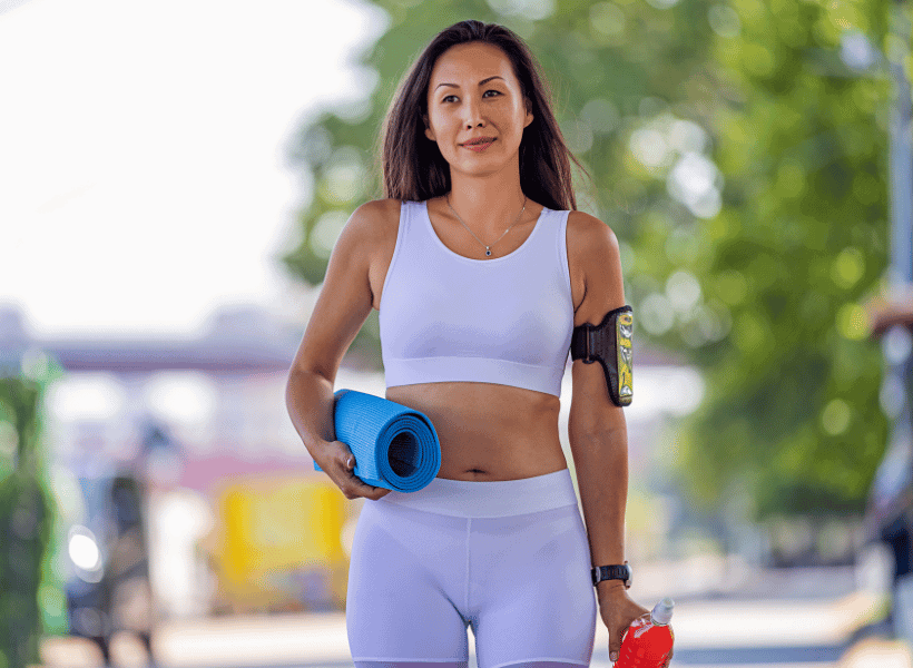 woman in white fitness clothing with yoga mat in one hand and a shaker bottle in the other hand