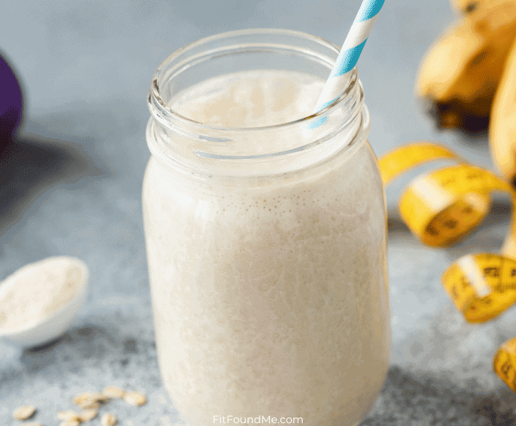 jar of protein shake with a straw with a measuring tape and weights laying beside it