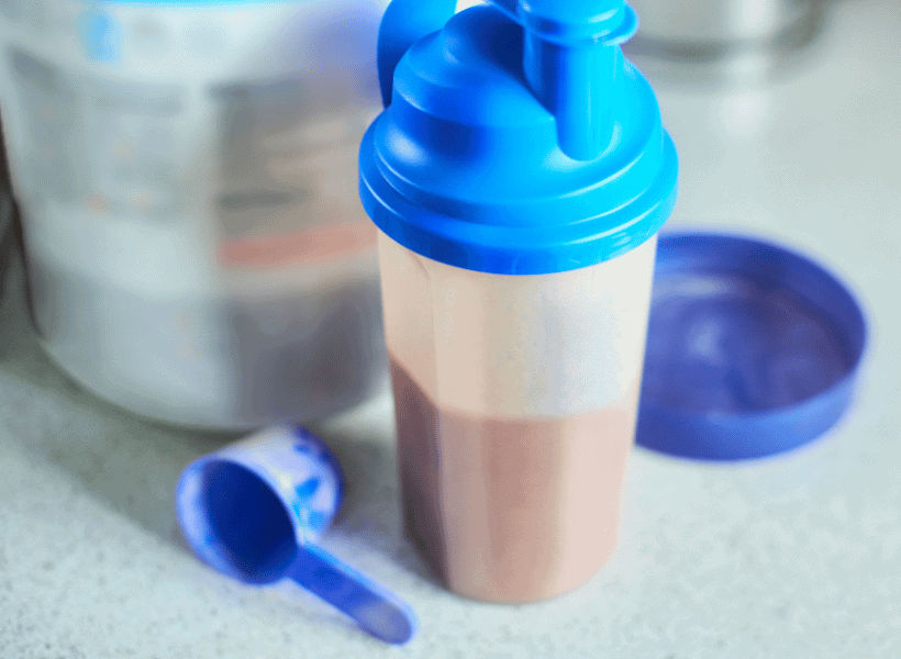 shaker bottle with chocolate meal replacement shake with scoop and container of powder beside it