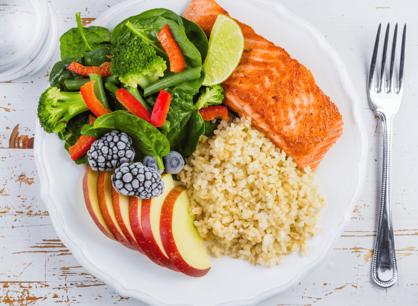 white plate on table with salmon, rice, sliced apple and vegetables.