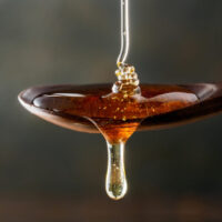 Honey,Pouring,On,Wooden,Spoon,And,Dripping,From,Spoon.,Dark